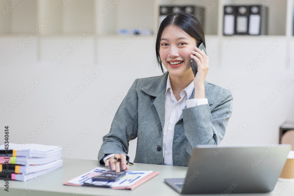 Smiling Asian business woman at work Call phone and working on laptop sitting at her working place in office, cheerful woman feel Excited and happy, copy space. Smiling Asian business woman at work Call phone and working on laptop sitting at her working place in office, cheerful woman feel Excited and happy, copy space.
