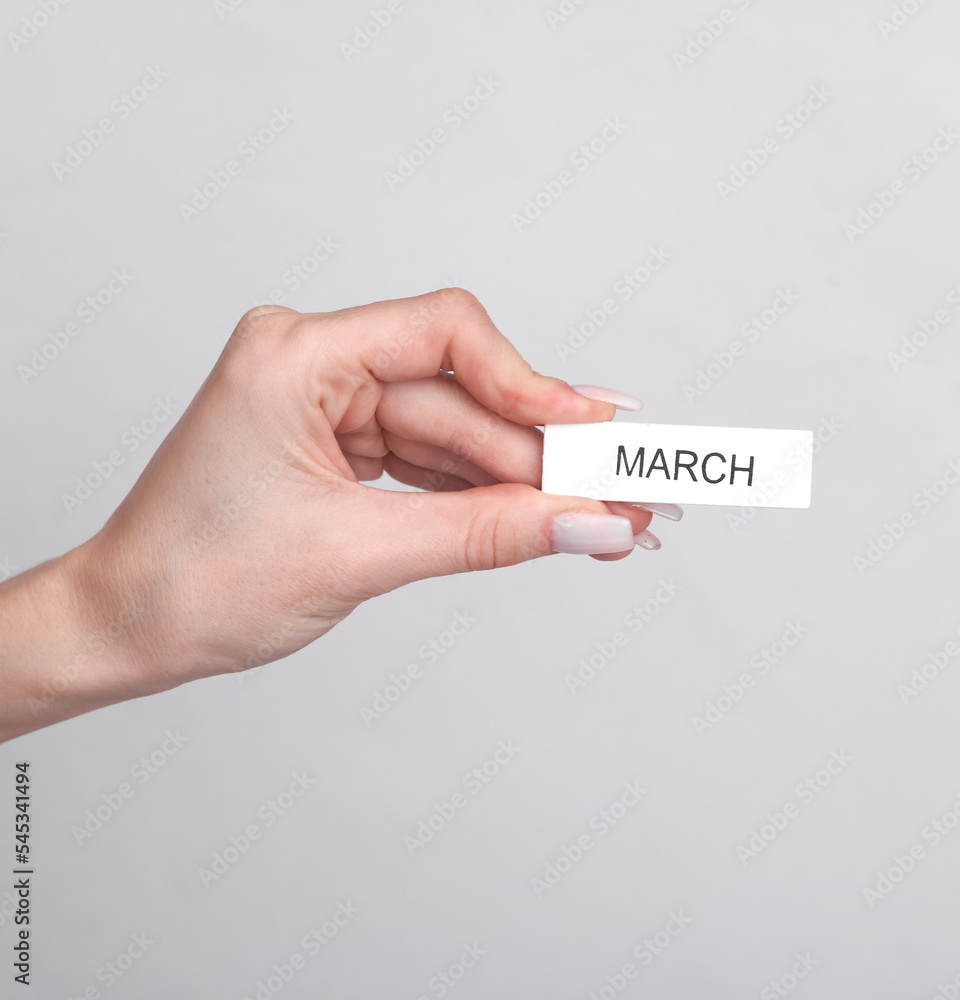 Woman's hand holds wooden white plate with inscription march on a gray background Woman's hand holds wooden white plate with inscription march on a gray background