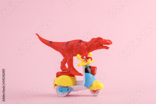 Toy red dinosaur tyrannosaurus rex ride on scooter, pink background. Minimalism creative layout.