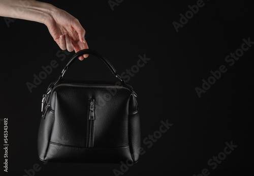 Female hand holding Black leather luxury handbag isolated on black background