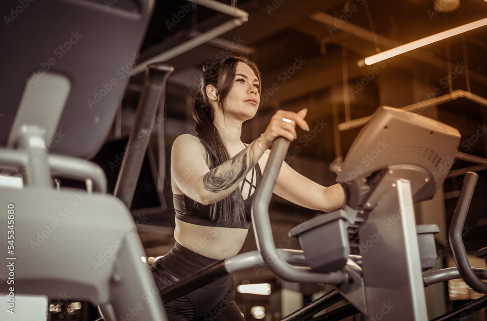 Young fitness woman doing cardo workout in exercise machine at the gym. Healthy lifestyle, sport concept Young fitness woman doing cardo workout in exercise machine at the gym. Healthy lifestyle, sport concept