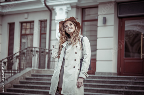 Portrait of cute smiling caucasian woman in hat and trench coat in the city