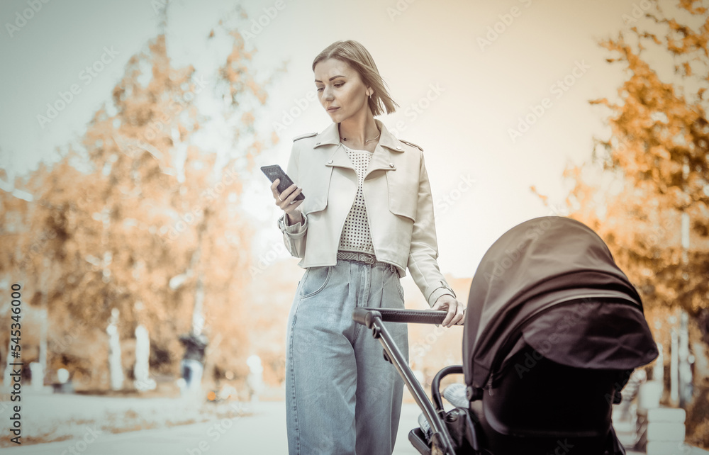 Stylish mom with stroller using smartphone in autumn park Stylish mom with stroller using smartphone in autumn park
