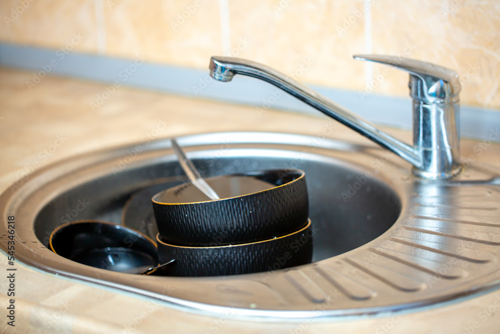 Obraz premium A pile of dirty dishes in the sink. Black dishes are stacked in a metal sink in the kitchen. Washing dishes, house cleaning.