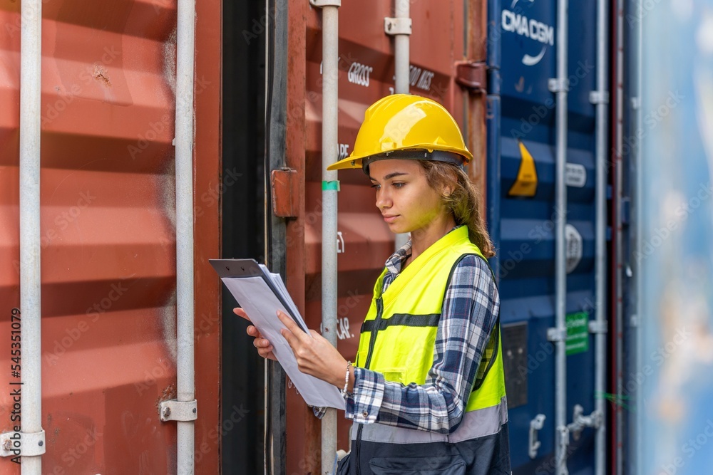 Photo of a young beautiful professional western female brunette engineer inspecting containers in a shipping containers yard to ensure the content and delivery information is correct Photo of a young beautiful professional western female brunette engineer inspecting containers in a shipping containers yard to ensure the content and delivery information is correct
