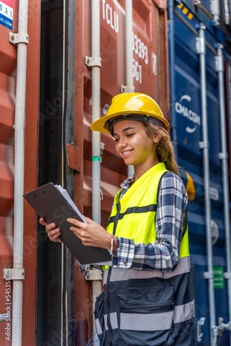 Photo of a young beautiful professional western female brunette engineer inspecting containers in a shipping containers yard to ensure the content and delivery information is correct