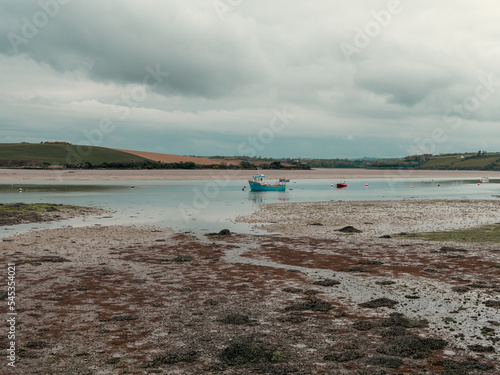 Clonakilty Bay at low tide on a day. A small blue fishing boat is anchored. Open seabed  silt and algae. Picturesque seaside landscape.