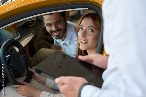 Joyous auto dealership customers communicating with sales consultant