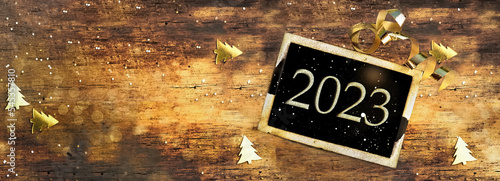 2023 written on  little board on rustic wooden background with golden confett...