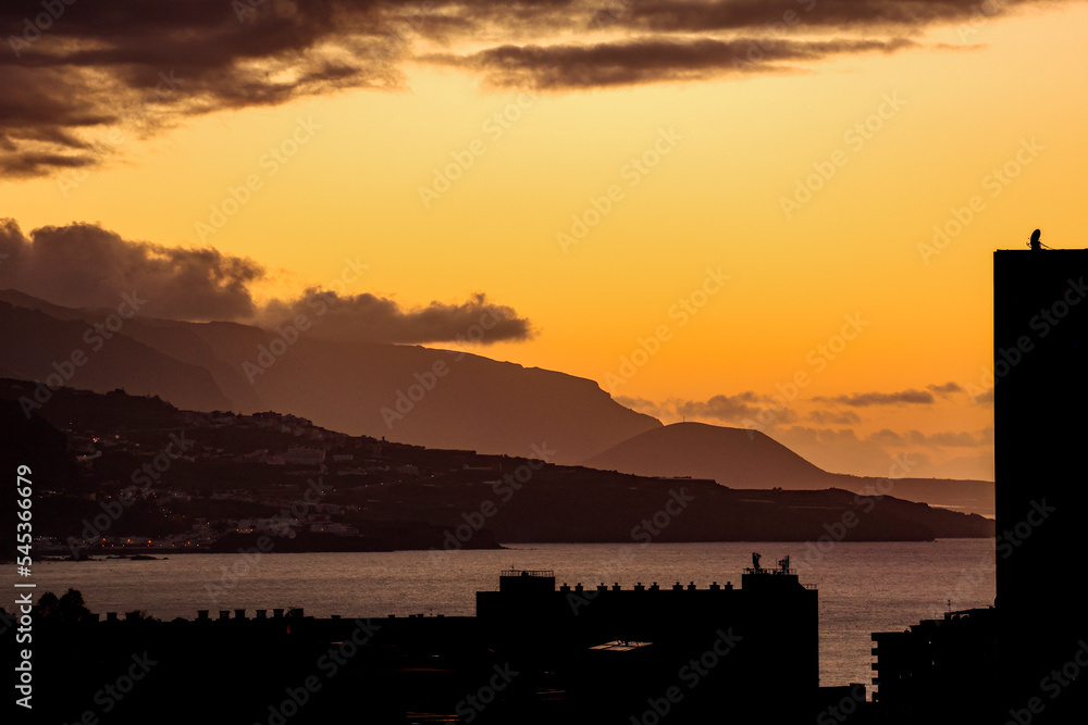 Bright yellow sunset in the island of Tenerife, Spain causing the city of Puerto de la Cruz to Silhouette in the foreground. 