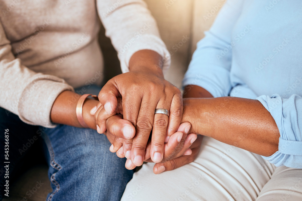 Support, love and closeup of people holding hands for comfort while sitting on a sofa together. Compassion, sympathy and friends praying, bonding and healing together in the living room of a house.