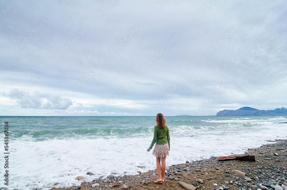 Vacation on the shore. Young woman standing on sea beach enjoying beautiful view.