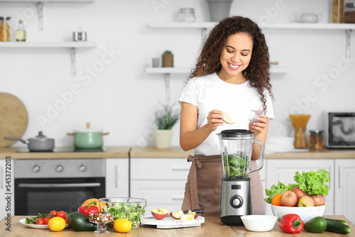 Young African-American woman making healthy smoothie in kitchen
