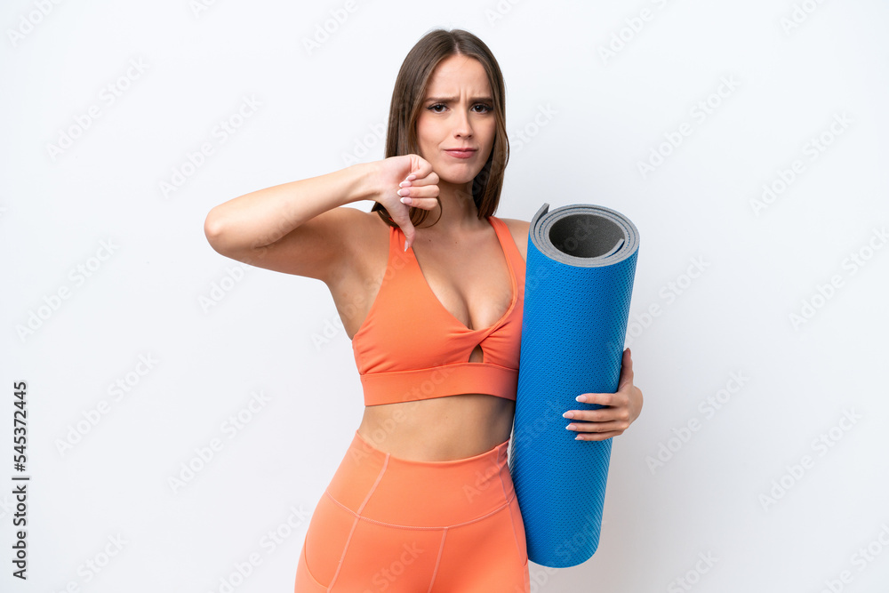 Young beautiful sport woman going to yoga classes while holding a mat isolated on white background showing thumb down with negative expression Young beautiful sport woman going to yoga classes while holding a mat isolated on white background showing thumb down with negative expression