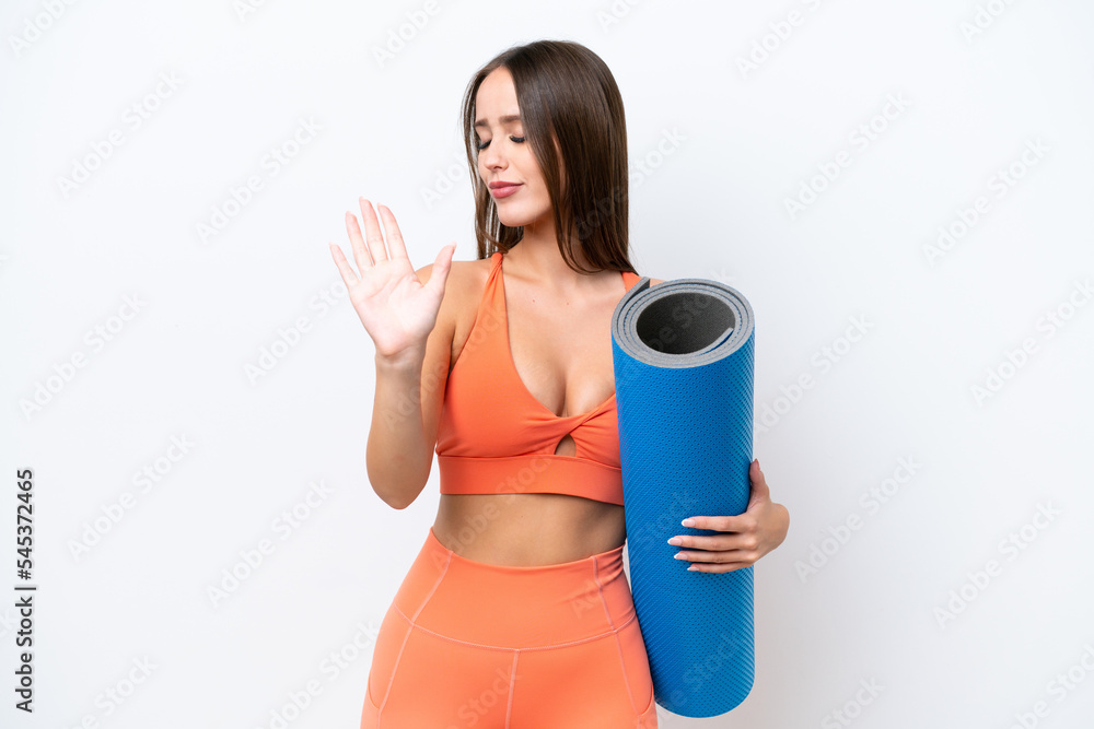 Young beautiful sport woman going to yoga classes while holding a mat isolated on white background making stop gesture and disappointed Young beautiful sport woman going to yoga classes while holding a mat isolated on white background making stop gesture and disappointed