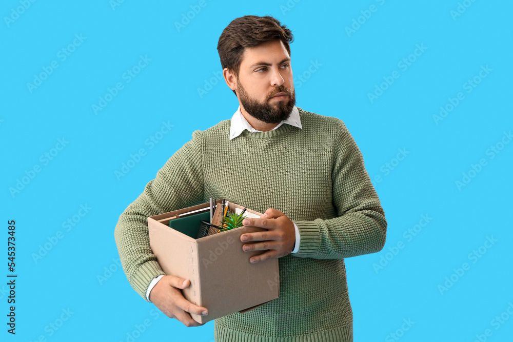 Fired young man holding box with personal stuff on blue background Fired young man holding box with personal stuff on blue background