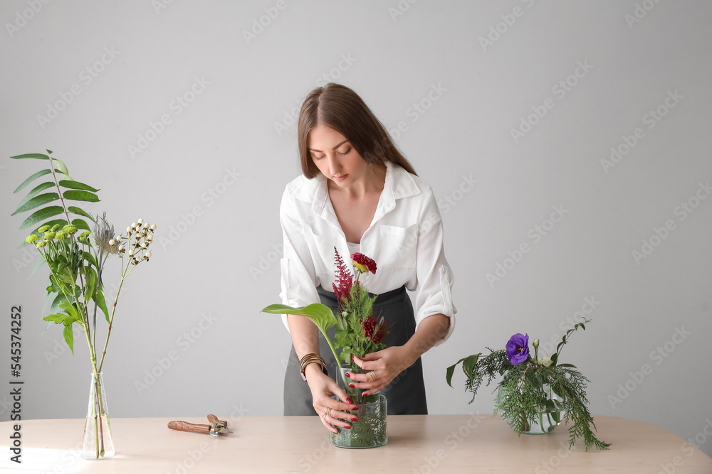 Young woman making beautiful ikebana at table near grey wall Young woman making beautiful ikebana at table near grey wall
