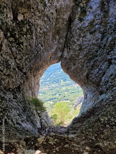 Scenic view to amazing cave in Slovenia at summer. View to green hills and forest. Natural backgrounds. Window in the rocks