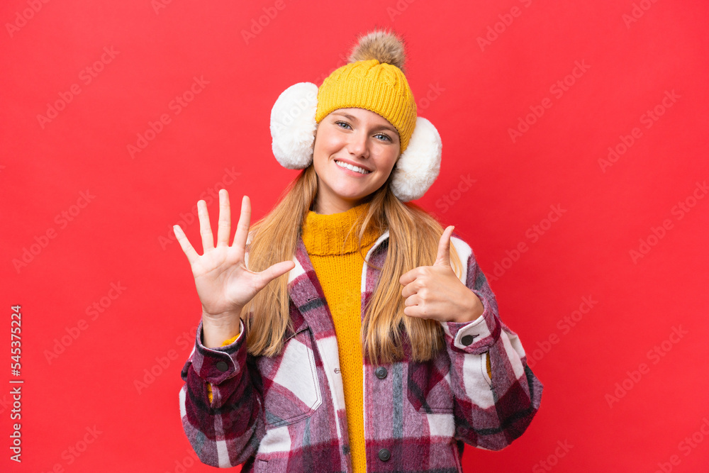 Young beautiful woman wearing winter muffs isolated on red background counting six with fingers Young beautiful woman wearing winter muffs isolated on red background counting six with fingers