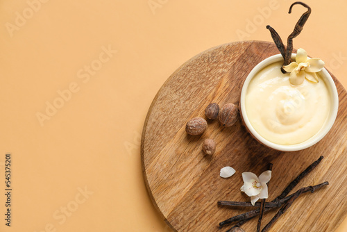 Fototapeta Board with ramekin of tasty pudding, vanilla sticks and nuts on beige background
