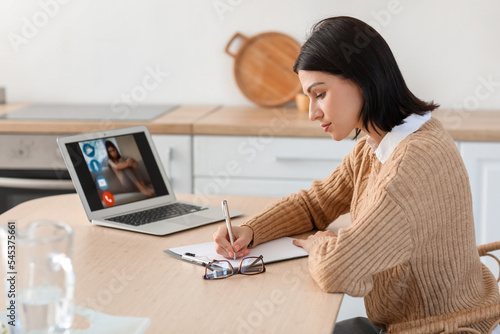 Female psychologist video chatting with patient in kitchen