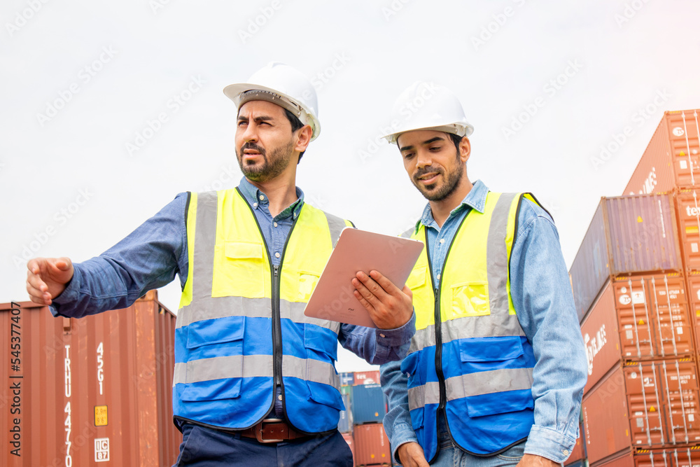 Two professional engineers in safety helmets and uniforms consulting each together in a container shipping company, a collaboration concept Two professional engineers in safety helmets and uniforms consulting each together in a container shipping company, a collaboration concept
