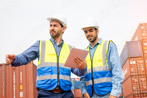 Two professional engineers in safety helmets and uniforms consulting each together in a container shipping company, a collaboration concept