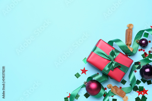 Composition with Christmas gift, balls, candies and confetti on color background