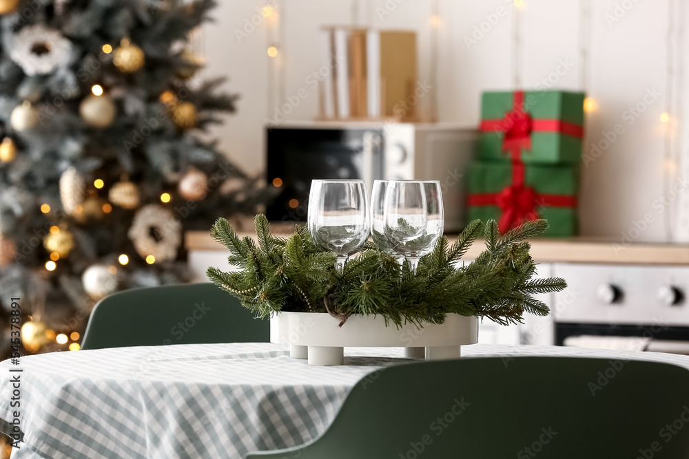 Stand with glasses and Christmas branches on dining table in kitchen