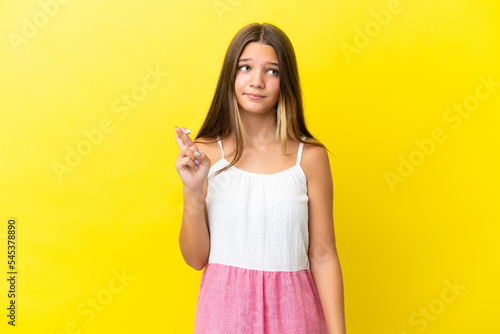 Little caucasian girl isolated on yellow background with fingers crossing and wishing the best