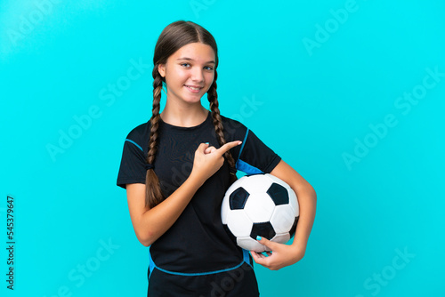 Little caucasian girl isolated on blue background with soccer ball and pointing to the lateral