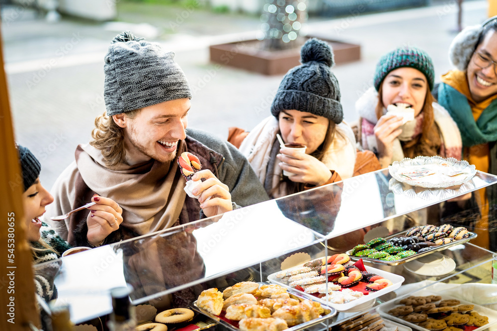 Obraz premium Happy friends having fun eating at Christmas market on winter holidays - Urban vacation concept with young people hanging out together by candy shop