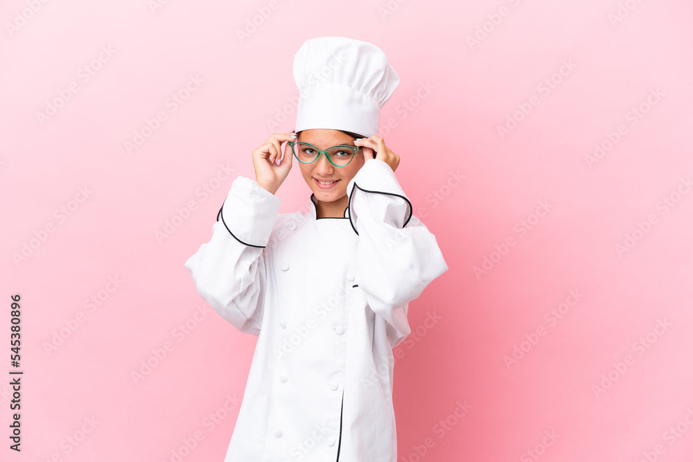 Little caucasian chef girl isolated on pink background with glasses and surprised Little caucasian chef girl isolated on pink background with glasses and surprised