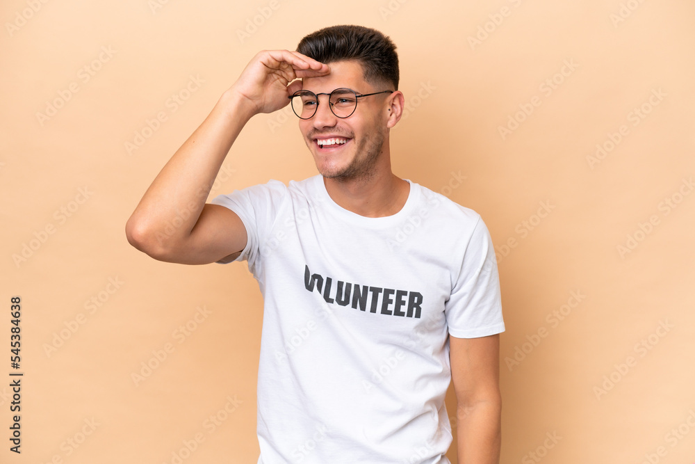 Young volunteer caucasian man isolated on beige background looking far away with hand to look something Young volunteer caucasian man isolated on beige background looking far away with hand to look something