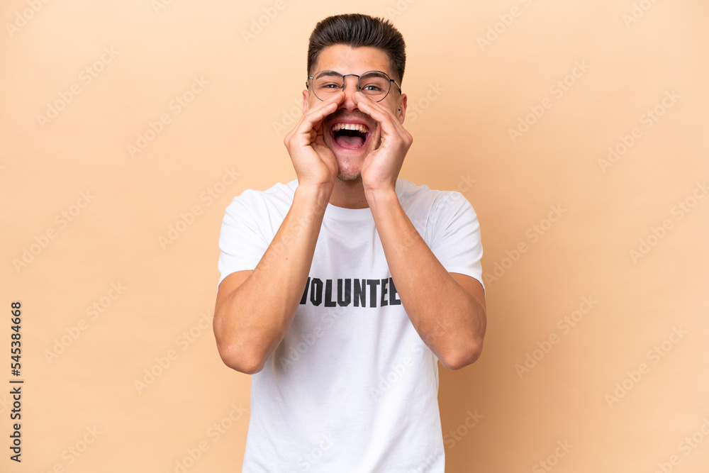 Young volunteer caucasian man isolated on beige background shouting and announcing something Young volunteer caucasian man isolated on beige background shouting and announcing something