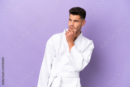Young caucasian man doing karate isolated on purple background and looking up © luismolinero