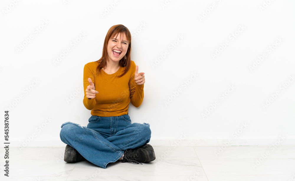 Redhead girl sitting on the floor isolated on white background pointing to the front and smiling Redhead girl sitting on the floor isolated on white background pointing to the front and smiling