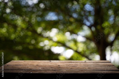 Empty wooden board on table top and blur inside abstract green background with natural bokeh, mock up for display of goods.