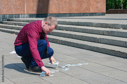 A businessman in a tie picks up a large amount of spilled money from the road