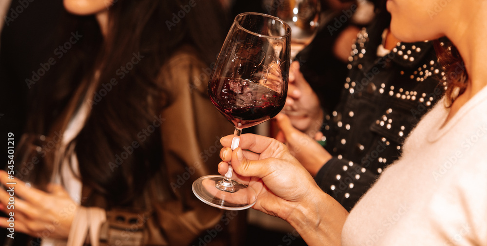 Glass of red wine held by a person at a premium wine tasting with friends and wine lovers.