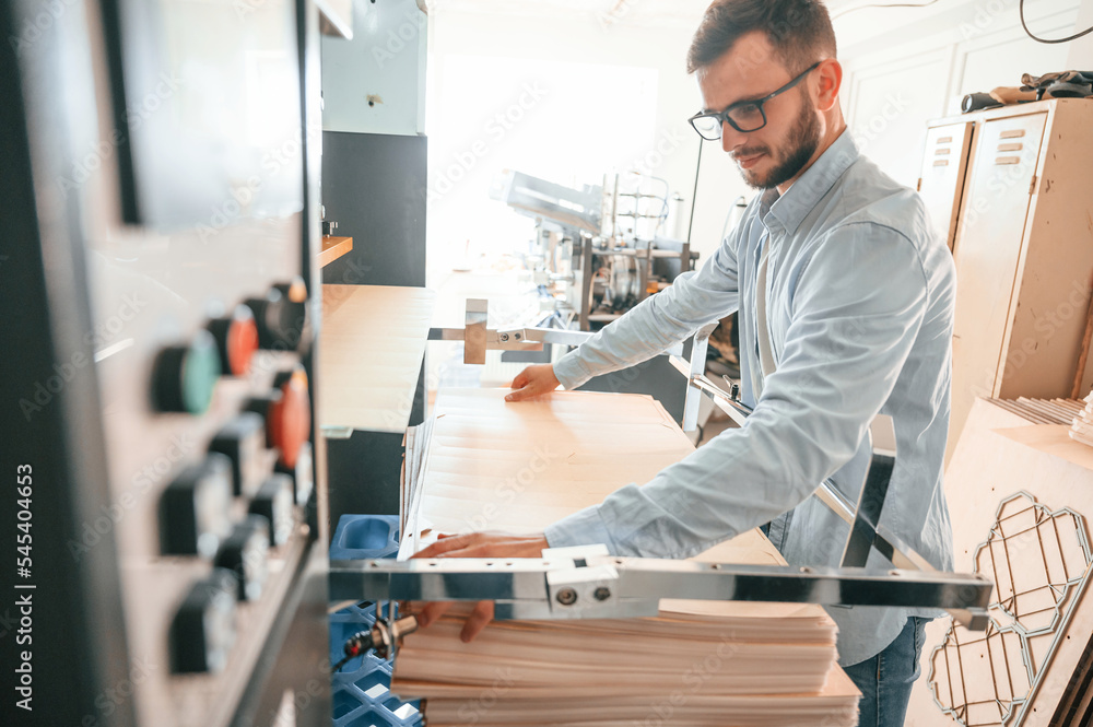 Working with wooden sheets. Man in print house that in white clothes is indoors Working with wooden sheets. Man in print house that in white clothes is indoors
