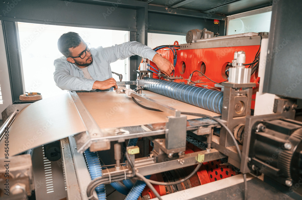 Sheet cutting machine. Operating device. Print house worker in white clothes is indoors Sheet cutting machine. Operating device. Print house worker in white clothes is indoors