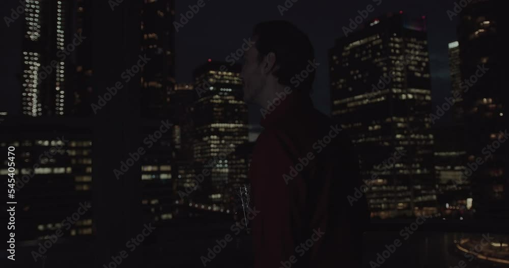 Adult Male Looking at City Skyline at Night Drinking from Glass Adult Male Looking at City Skyline at Night Drinking from Glass