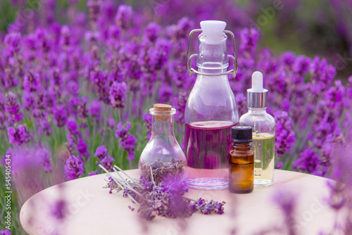 A bottle of lavender essential oil on a wooden table and a field of flowers background.