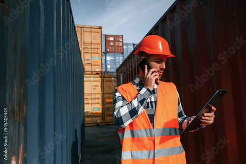Having conversation by phone. Male worker is on the location with containers