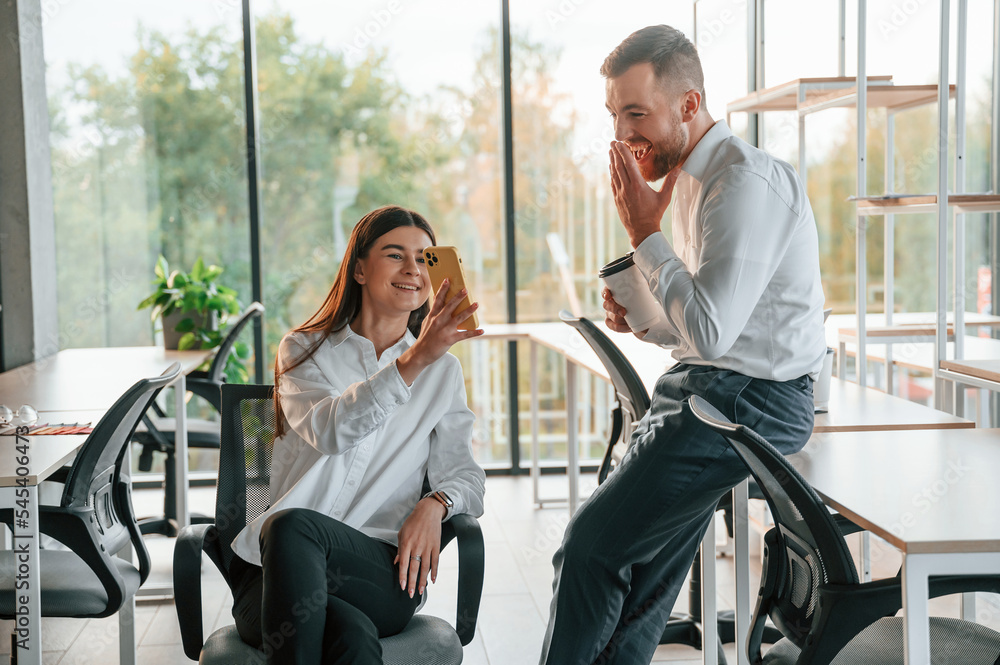 Having a break, talking, using smartphone. Man and woman are working in the modern office together Having a break, talking, using smartphone. Man and woman are working in the modern office together