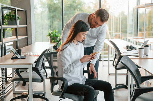 Showing something on the smartphone. Man and woman are working in the modern office together