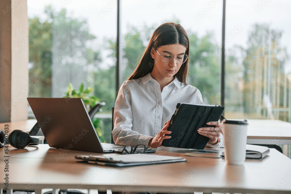 Using tablet. Beautiful young woman in white clothes is working in office