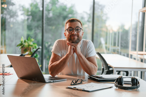 Smilling and sitting. Positive man in formal clothes is working in the modern office