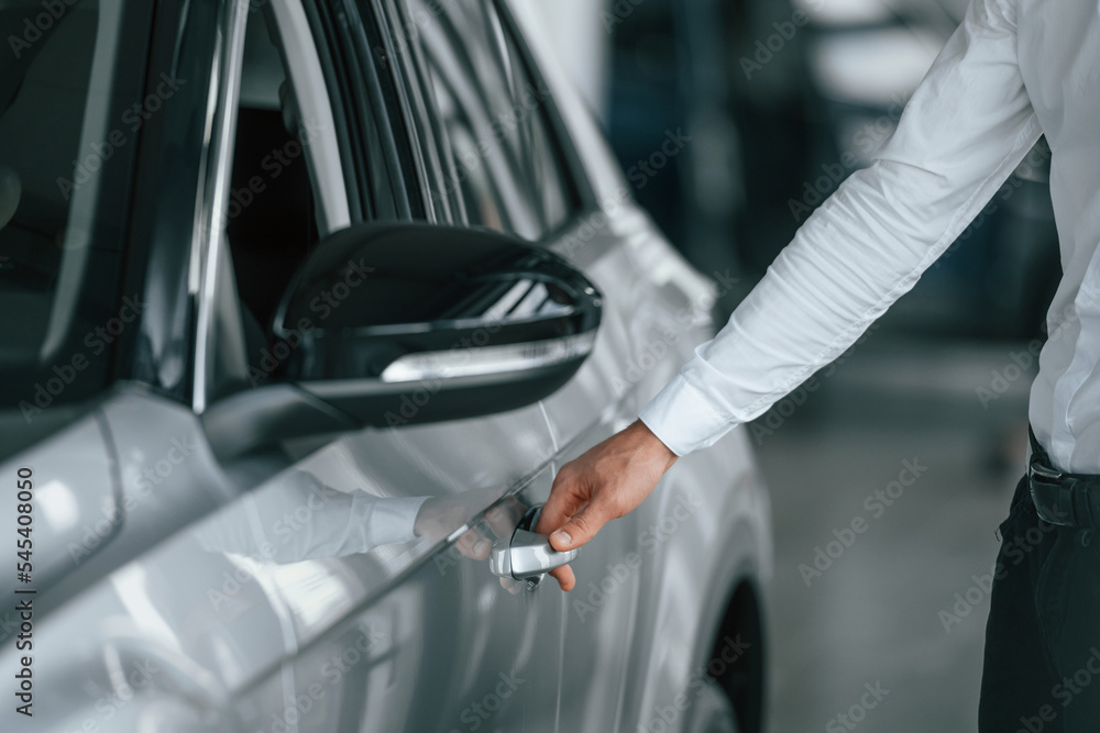 Opening the door. Young man in white clothes is in the car dealership Opening the door. Young man in white clothes is in the car dealership